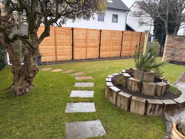 Modernisierung eines Bestandsgartens mit individuellem Holzzaun - Illertissen Ein Garten mit einem Steg, einer Steinmauer und einer kleinen Wasserstelle.